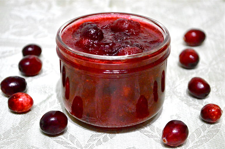 A jar of festive homemade cranberry sauce with a few fresh cranberries scattered around.