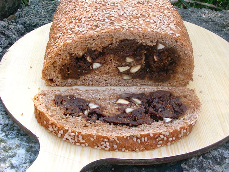 A slice from a figgy bread roll wholemeal loaf covered in sesame seeds.