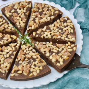 A plate with eight slices of castagnaccio, a simple Italian chestnut cake topped with nuts.