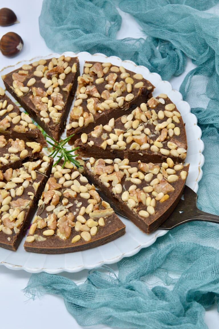 A plate with eight slices of castagnaccio, a simple Italian chestnut cake topped with nuts.