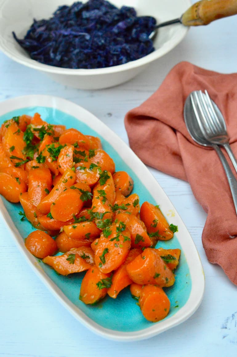 A platter of honey butter glazed carrots with a bowl of red cabbage in the background.