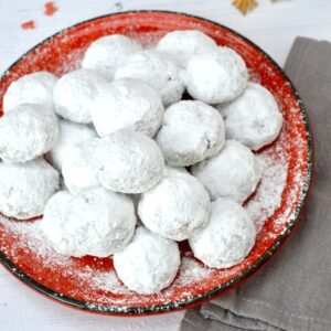 Pecan snowball cookies piled on a red plate.