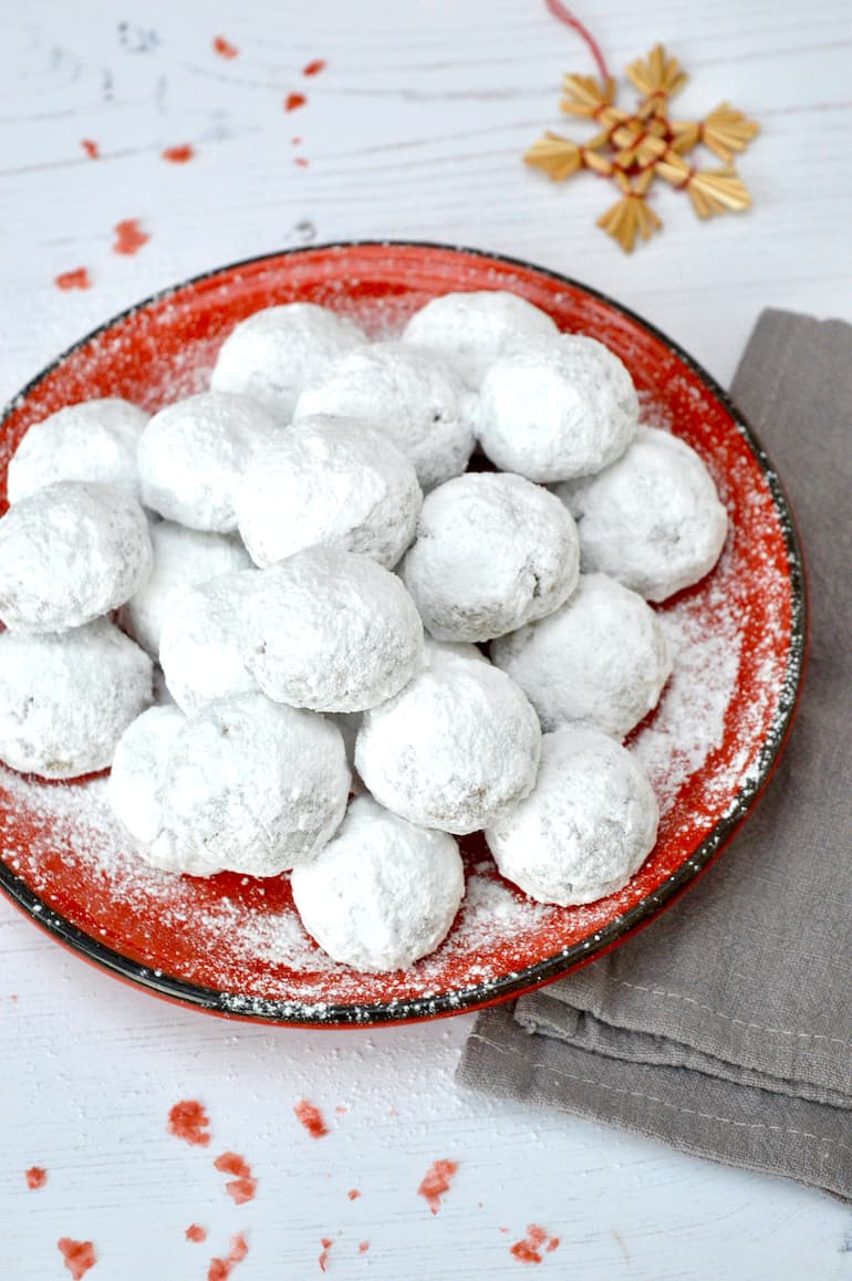 Pecan snowball cookies piled on a red plate.