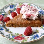A slice of almond rye shortbread on a plate with raspberry whisky cream and raspberries.