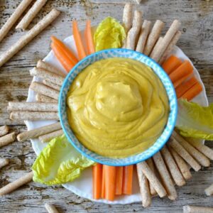 A bowl of cheesy cashew nut sauce (or dip) with breadsticks and crudités.
