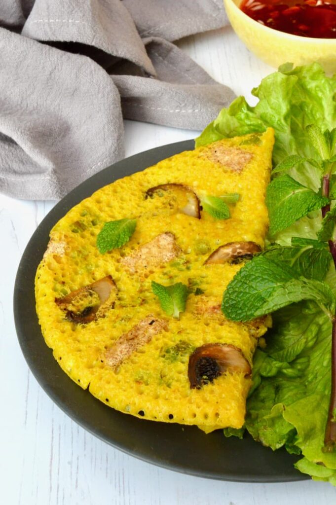 Vegan bánh xèo, a savoury Vietnamese pancake on a plate with lettuce and mint.