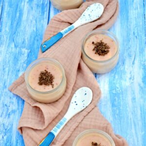 Four pots of blood orange posset arranged on a cloth with two blue spoons.