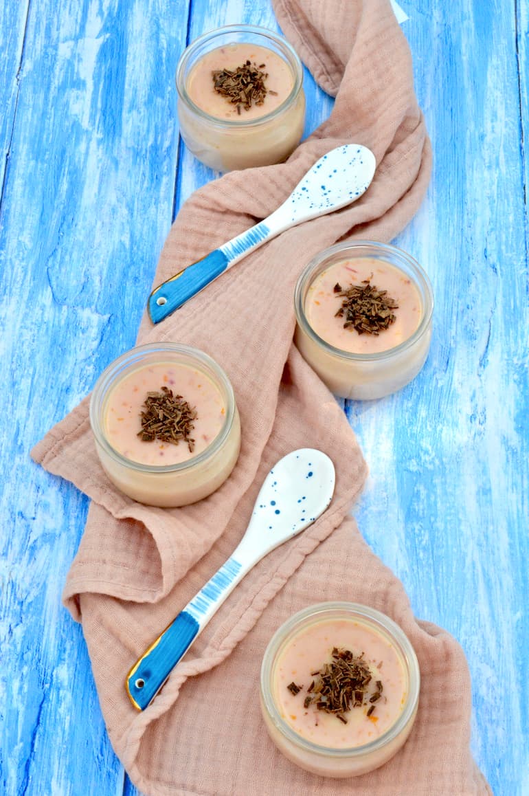 Four pots of blood orange posset arranged on a cloth with two blue spoons.