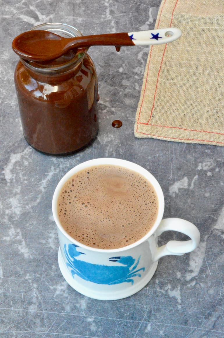 A cup of vegan hot chocolate with a jar of homemade chocolate sauce behind.
