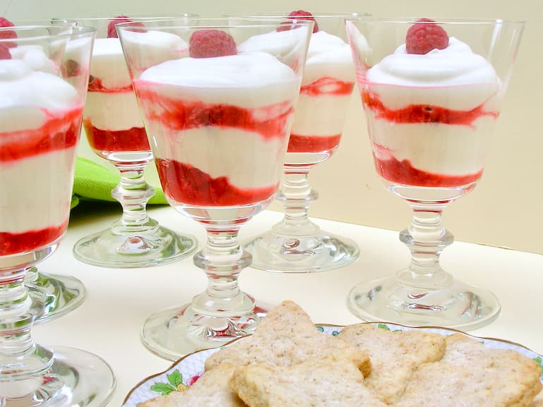 Glasses of layered raspberry syllabub with a plate of Chardonnay vanilla biscuits.