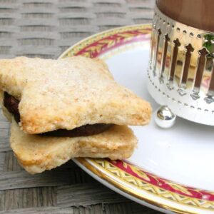 Vanilla biscuit sandwiched with chocolate ganache on the side of a plate containing a glass of hot chocolate.