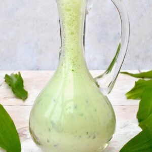 A glass salad oil jug filled with creamy wild garlic dressing.