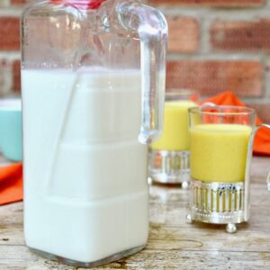 A jug of homemade milk kefir with two glasses of kefir drinks behind. Part of the post: How to Make Kefir and What to Do With It.
