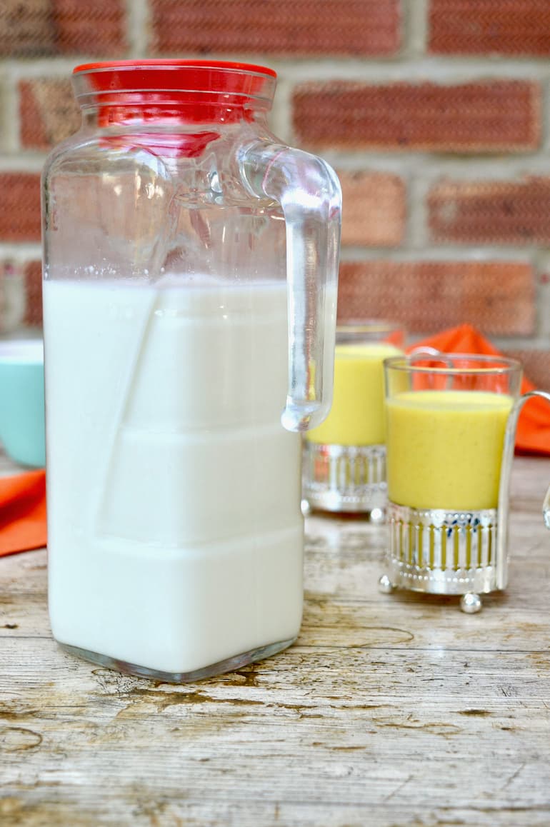 A jug of homemade milk kefir with two glasses of kefir drinks behind. Part of the post: How to Make Kefir and What to Do With It.