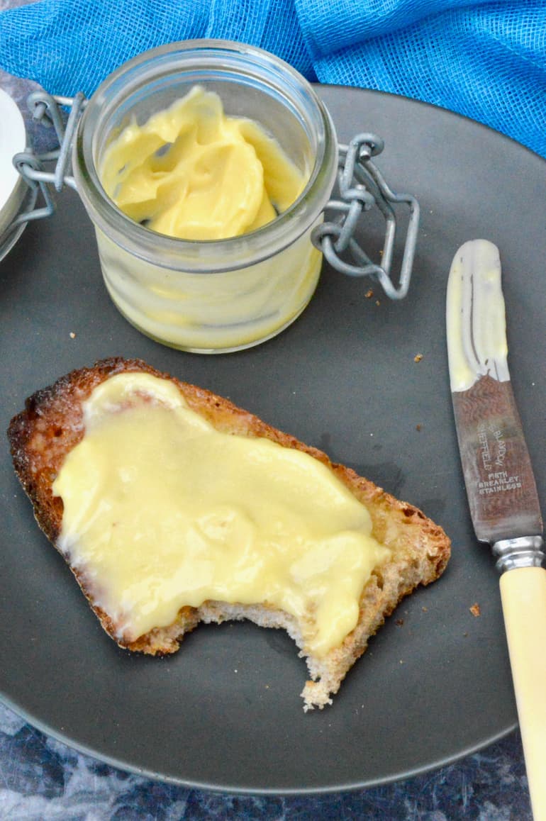 Homemade lemon curd on toast with a jar of it behind.