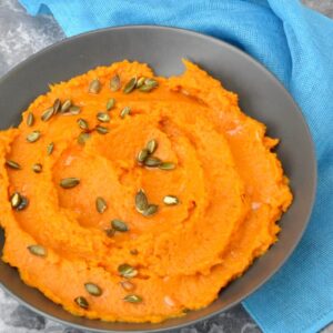 A bowl of dairy-free sweet potato mash scattered with toasted pumpkin seeds.