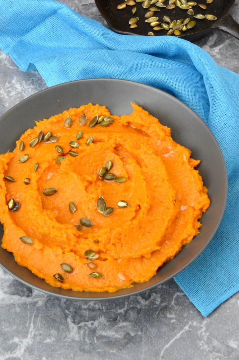 A bowl of dairy-free sweet potato mash scattered with toasted pumpkin seeds.