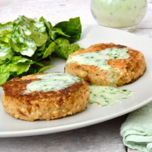 Two homemade white bean burgers on a plate with green leaves and creamy wild garlic dressing.