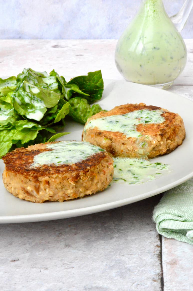Two homemade white bean burgers on a plate with green leaves and creamy wild garlic dressing.