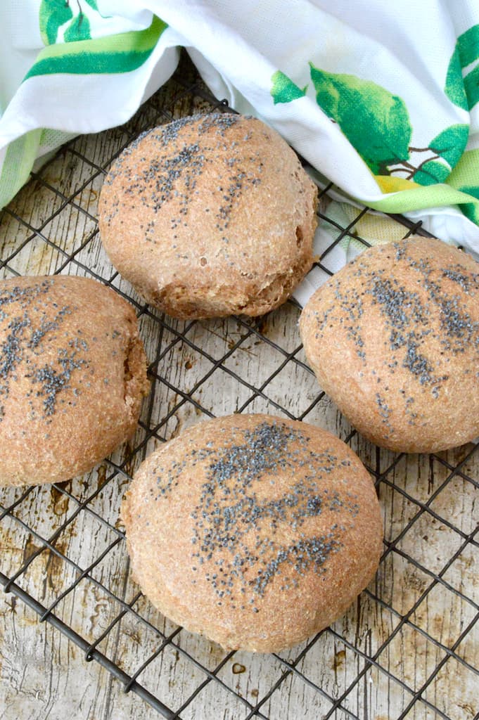 Four wholemeal sourdough bread rolls with poppy seeds on top cooling on a rack.