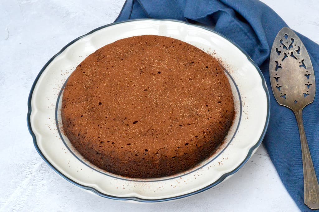 Chocolate polenta cake on a plate with cake slice to one side.