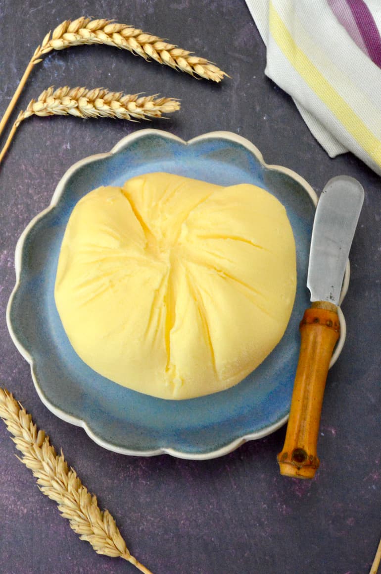 A ball of homemade butter on a plate with butter knife.