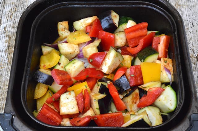 An air fryer drawer filled with chopped summer veg.