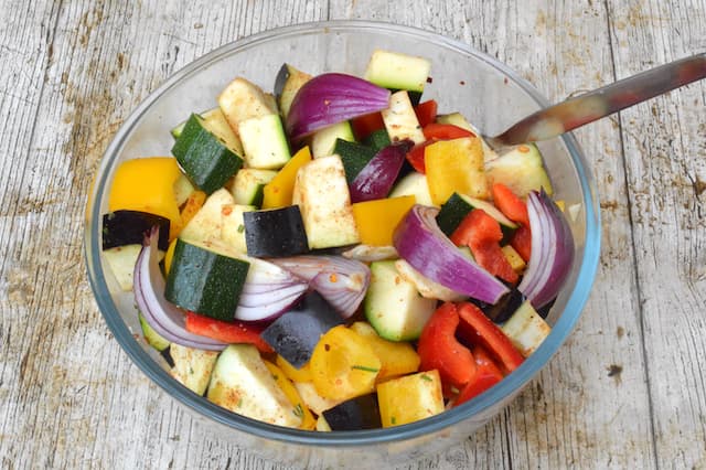 A bowl of chopped summer veg mixed with spices and oil.