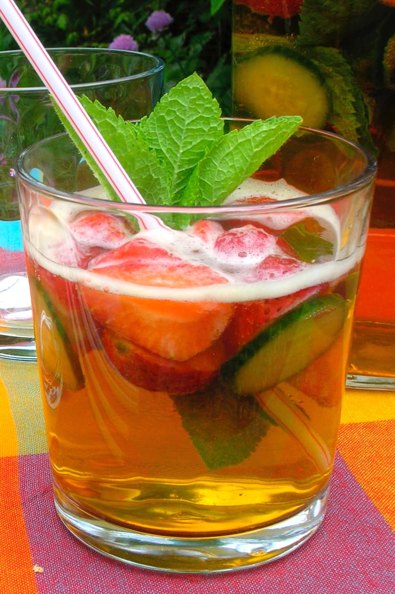 A glass of Pimms No 1 cocktail with strawberries, cucumber, mint and a straw.