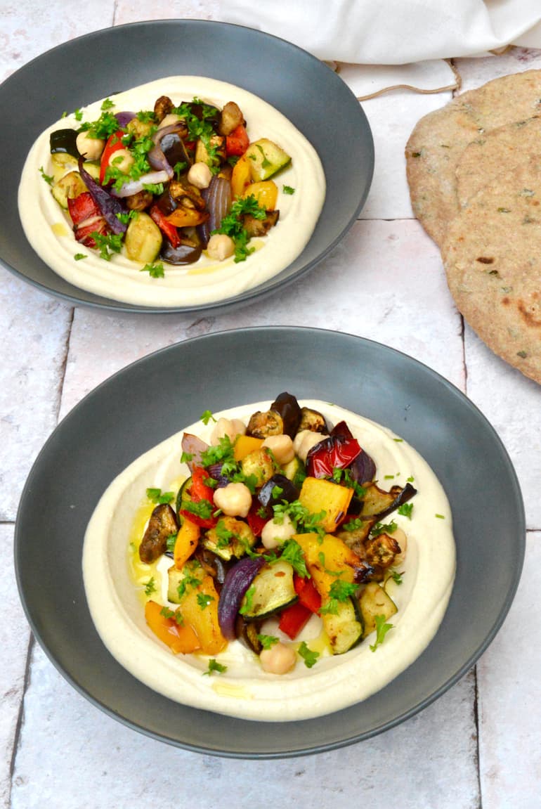 Two bowls of roasted Mediterranean vegetables with hummus.