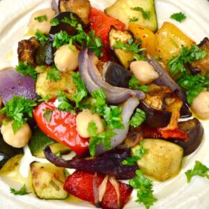 Close up of a bowl of roasted Mediterranean vegetables on a bed of hummus.