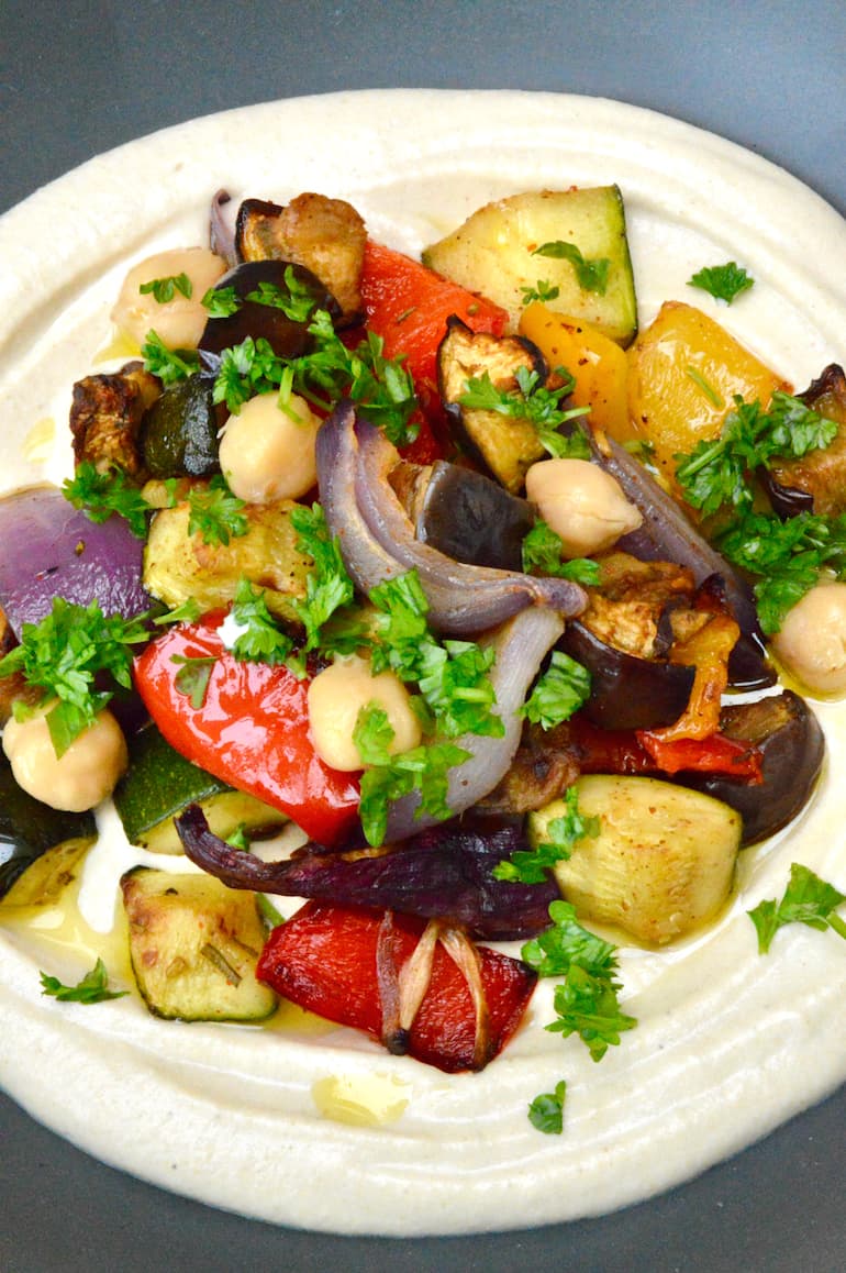 Close up of a bowl of roasted Mediterranean vegetables on a bed of hummus.