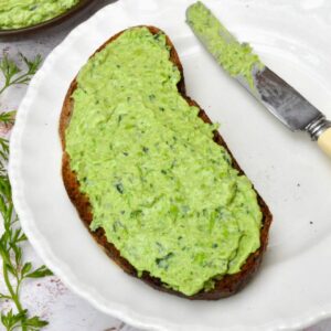 Creamy pea dip with fresh herbs spread on a slice of toast.