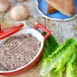 A red dish of vegan mushroom pâté with toast, lettuce and whole mushrooms.