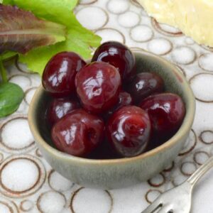 A bowl of easy homemade pickled cherries with cheese and salad leaves.