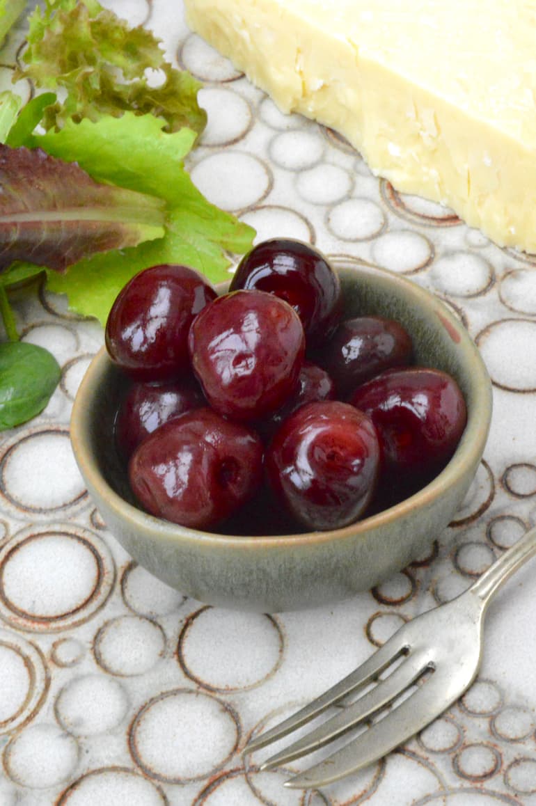 A bowl of easy homemade pickled cherries with cheese and salad leaves.