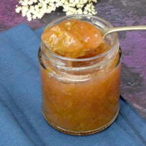 A jar of gooseberry and elderflower jam with a spoonful sitting on top.
