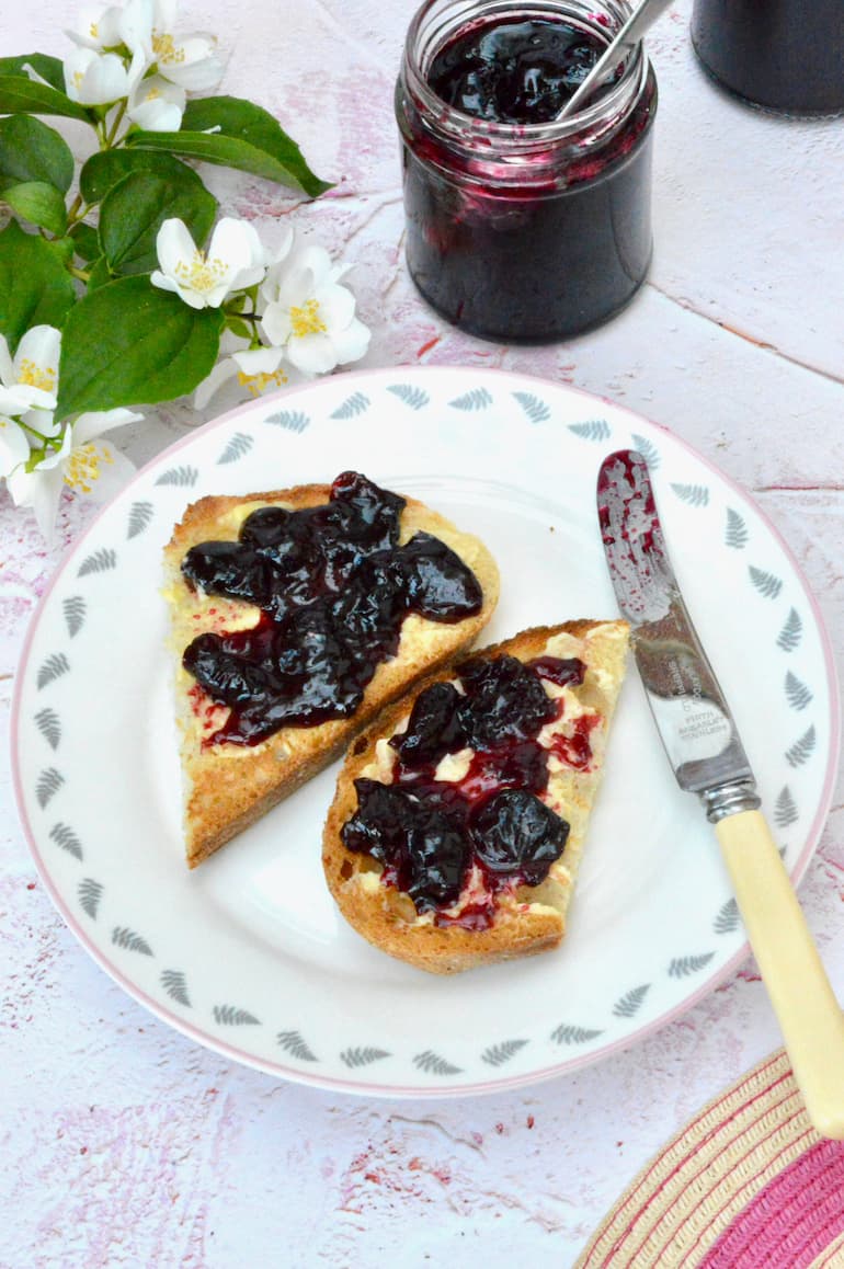 A plate of homemade cherry jam on toast with jar behind.