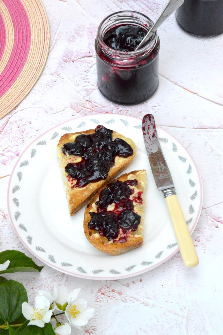 Homemade cherry jam on toast with a jar and spoon behind.