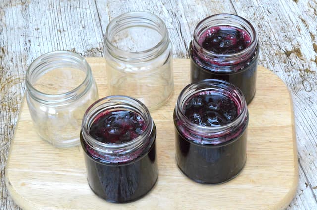Three open jars of hot cherry jam and two empty jars.