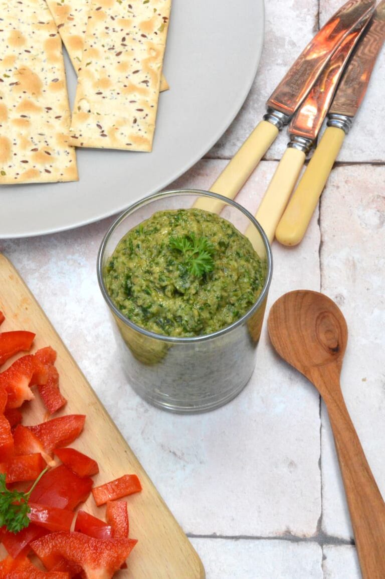 An open jar of Italian green sauce (bagnèt vert) with wooden spoon, knives and crackers.