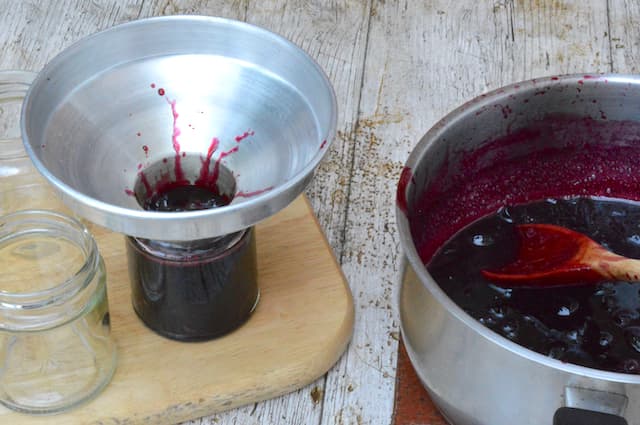 Cherry jam being jarred with a funnel.