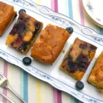 Five caramelised blueberry blondies on a rectangular serving plate.