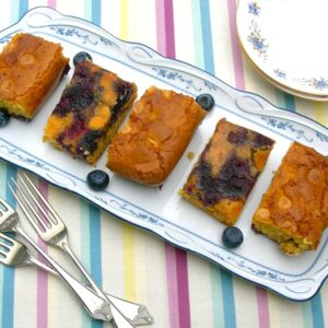 Five caramelised blueberry blondies laid out on a plate for afternoon tea.