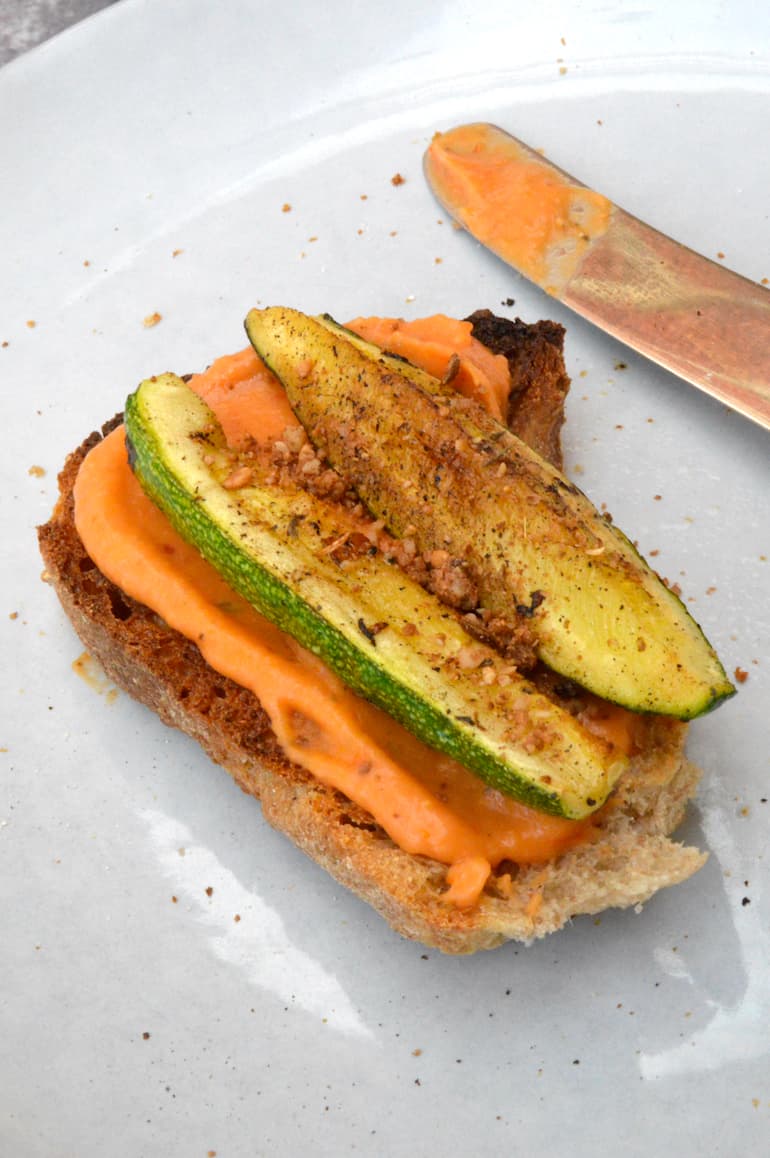 Roasted tomato and white been dip on toast with fried courgettes and knife.