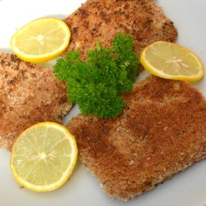3 pieces of vegan tofu schnitzel on a plate with slices of lemon and a sprig of parsley.