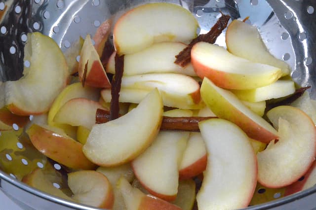 Poached sliced apples draining in colander.