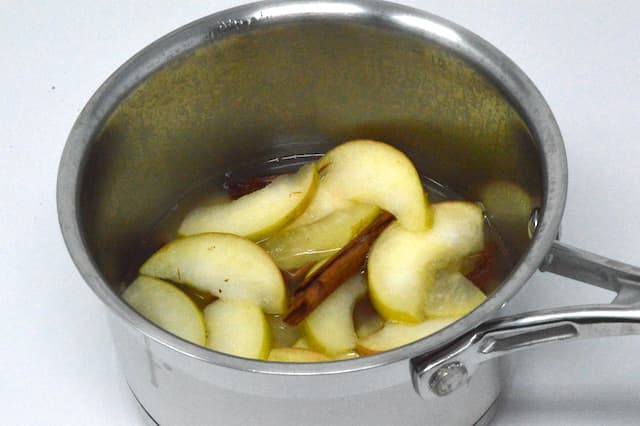 Sliced apples poaching with cinnamon stick.
