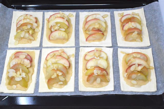 Poached apple slices and flaked almonds on raw pastry rectangles.