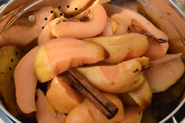 Unpeeled poached quince quarters draining in colander.